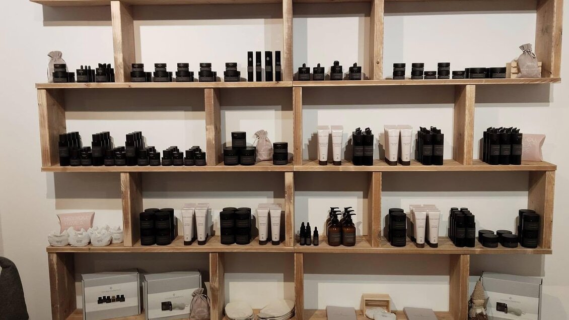 Ein Regal aus Holz mit verschiedenen Flaschen und Behältern für kosmetische Produkte. Die Anordnung ist ordentlich und modern, mit einigen Dekorationsobjekten. | © Verena Schmid