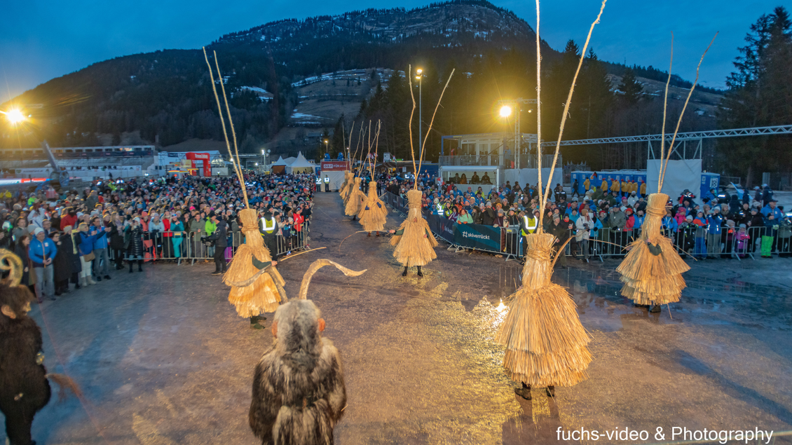 Eine festliche Veranstaltung mit einer großen Menschenmenge. Tänzer in traditionellen Kostümen führen eine Aufführung unter einem Abendhimmel auf. | © Manfred Fuchs