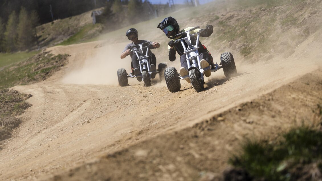 Zwei Kinder fahren mit Elektro-Karts auf einem staubigen Pistenweg. Im Hintergrund sind Bäume und Berge sichtbar. | © Oststeiermark Tourismus
