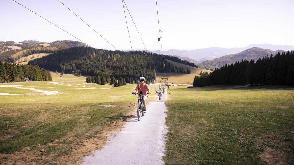Ein Radfahrer auf einem schmalen Weg in einer grünen Landschaft. Im Hintergrund sind Berge und Wälder zu sehen. | © Oststeiermark Tourismus
