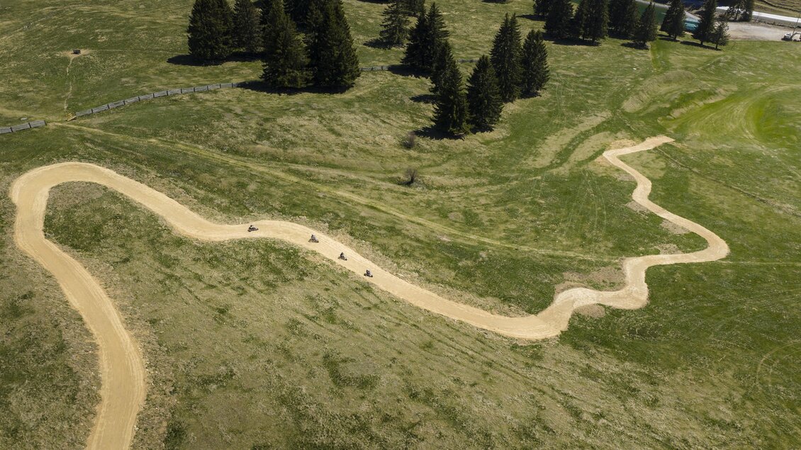 Eine kurvenreiche Strecke aus Sand durch grüne Wiesen. Im Hintergrund stehen einige hohe Tannenbäume. | © Oststeiermark Tourismus
