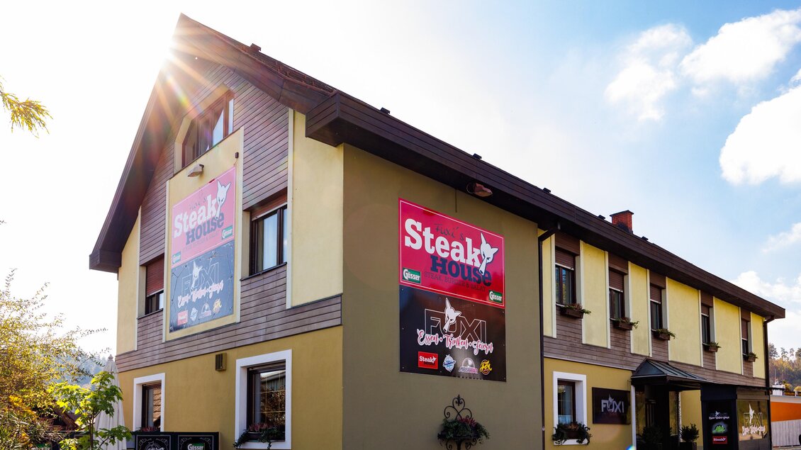 Außenansicht des Fuxi's Steakhouse in Bärnbach mit klarer Wetterlage und sichtbaren Werbeschildern des Restaurants. | © TV Region Graz - Harry Schiffer