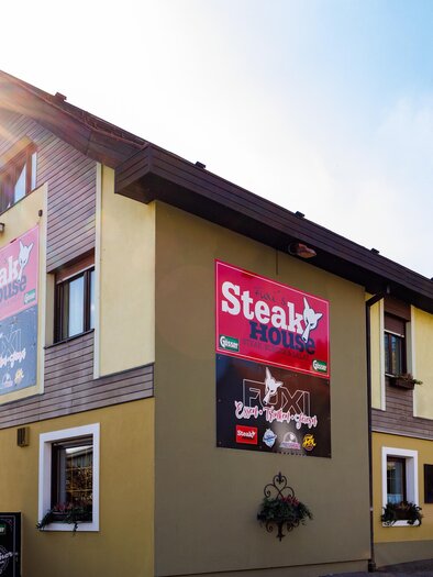 Außenansicht des Fuxi's Steakhouse in Bärnbach mit klarer Wetterlage und sichtbaren Werbeschildern des Restaurants. | © TV Region Graz - Harry Schiffer