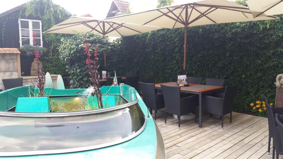 Ein grünes Motorboot steht im Gastgarten von Fuxi's Steakhouse in Bärnbach, umgeben von Tischen, Stühlen und Sonnenschirmen.  | © TV Lipizzanerheimat/EU