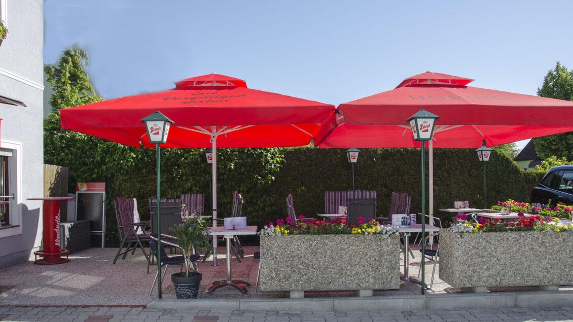 Gemütliche Terrasse des Gästehauses Café Andrea in Köflach-Pichling mit roten Sonnenschirmen und Blumenbeeten, ideal für entspannte Stunden im Freien. | © Hans Wölkart, Gästehaus Andrea