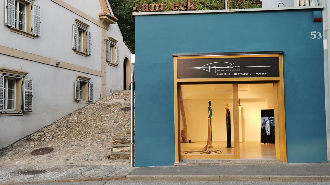 Ein modernes Geschäft mit einer blauen Fassade und großen Fenstern. Im Hintergrund ist eine steile Straße mit alten Gebäuden zu sehen. | © Jörg Roskaric