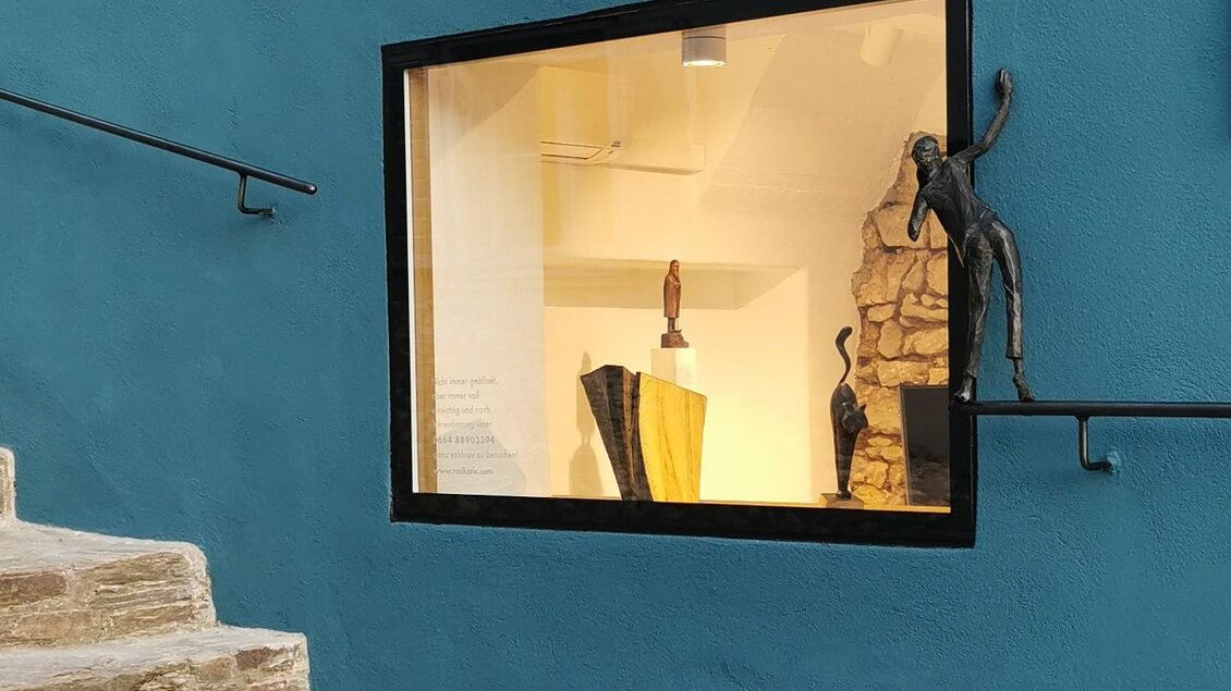 Ein modernes Schaufenster mit verschiedenen Skulpturen ist sichtbar. Die Wand ist in einem kräftigen Blauton gestrichen und es gibt Treppenstufen im Vordergrund. | © Jörg Roskaric