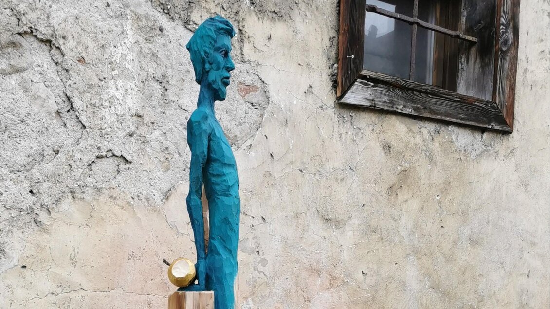 Eine skulpturale Figur in Blau steht an einer Wand. Neben der Figur befindet sich ein goldenes Objekt. | © Jörg Roskaric