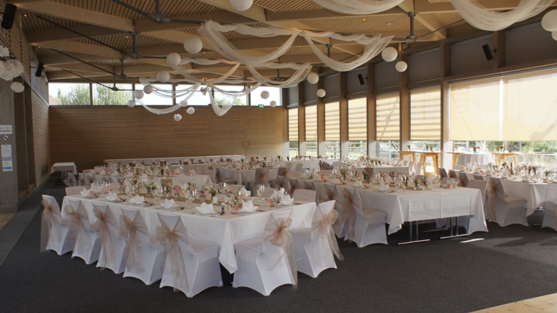 Ein festlich dekorierter Saal mit mehreren Tischen, die für ein Event gedeckt sind. Die Tische sind mit weißen Tischdecken und zarten Schleifen geschmückt. | © Oststeiermark Tourismus