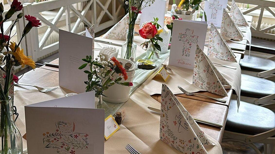Ein festlich gedeckter Tisch mit Blumen und hübsch gefalteten Servietten. Die Umgebung wirkt gemütlich und einladend. | © Gasthaus Bachwirt
