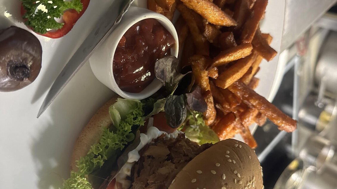 Ein leckerer Burger mit Sesambrötchen, frischem Gemüse und einer Beilage aus Süßkartoffelpommes. Dazu gibt es Ketchup und eine kleine Portion Salat. | © Gasthaus Bachwirt