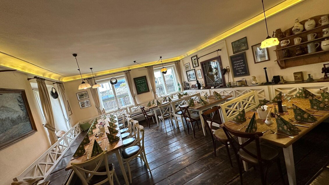 Ein gemütlicher Speisesaal mit langen Tischen und festlich dekorierten Tischen. Die Wände sind mit Bildern und Erinnerungsstücken geschmückt. | © Gasthaus Bachwirt