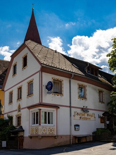 Außenansicht des Gasthauses Gangl in Ligist mit markantem Giebel, Gastgarten und angrenzender Kirche. | © TV Region Graz - Harry Schiffer