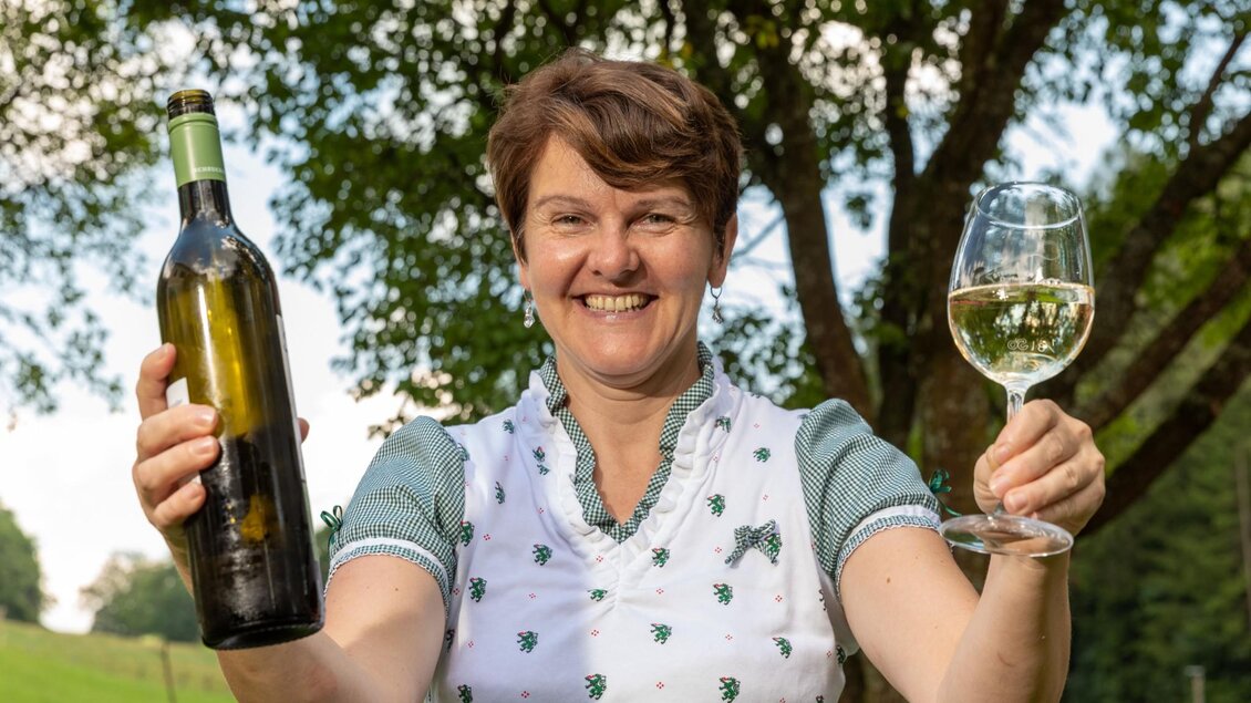 Frau im Freien hält eine Weinflasche und ein Glas Weißwein im Häuserl im Wald in Semriach | © TV Region Graz - Harry Schiffer