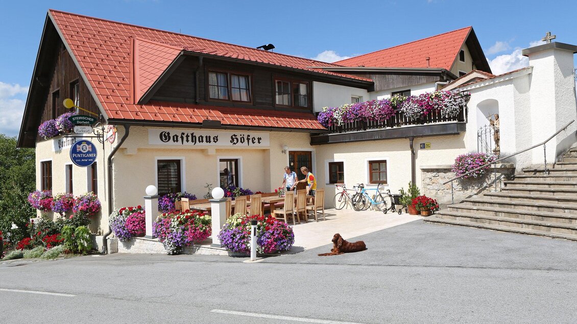 Ein einladendes Gasthaus mit bunten Blumenkästen und einer gemütlichen Terrasse. Fahrräder stehen bereit und ein Hund liegt entspannt davor. | © TV Region Graz - Donner