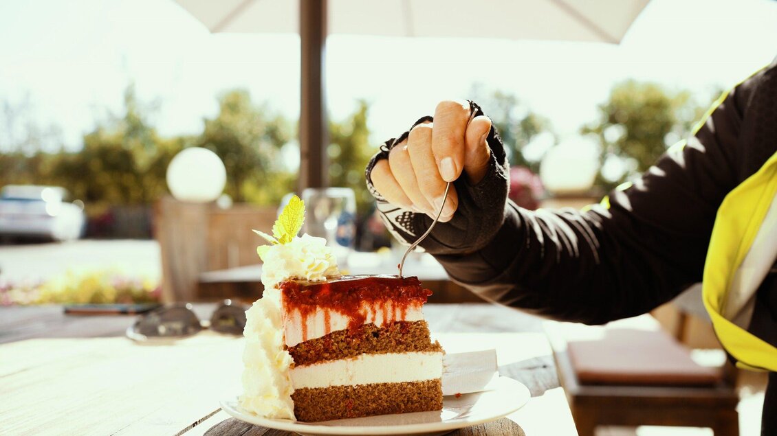 Ein Stück Kuchen mit Sahne und Fruchtsoße wird genossen. Die Hand einer Person hält einen Löffel, während sie ein Stück herausschneidet. | © TV Region Graz - Mias Photoart