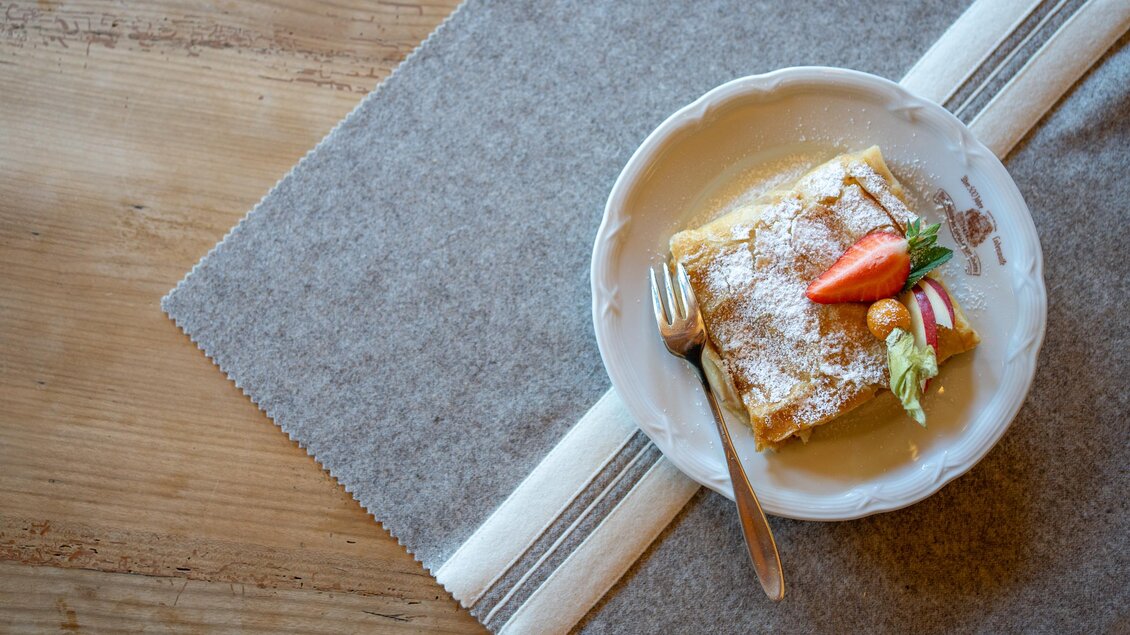 Ein Topfenstrudel mit Puderzucker und Obstgarnitur auf einem weißen Teller. | © Alwin Strasser | Lodenwalker Ramsau