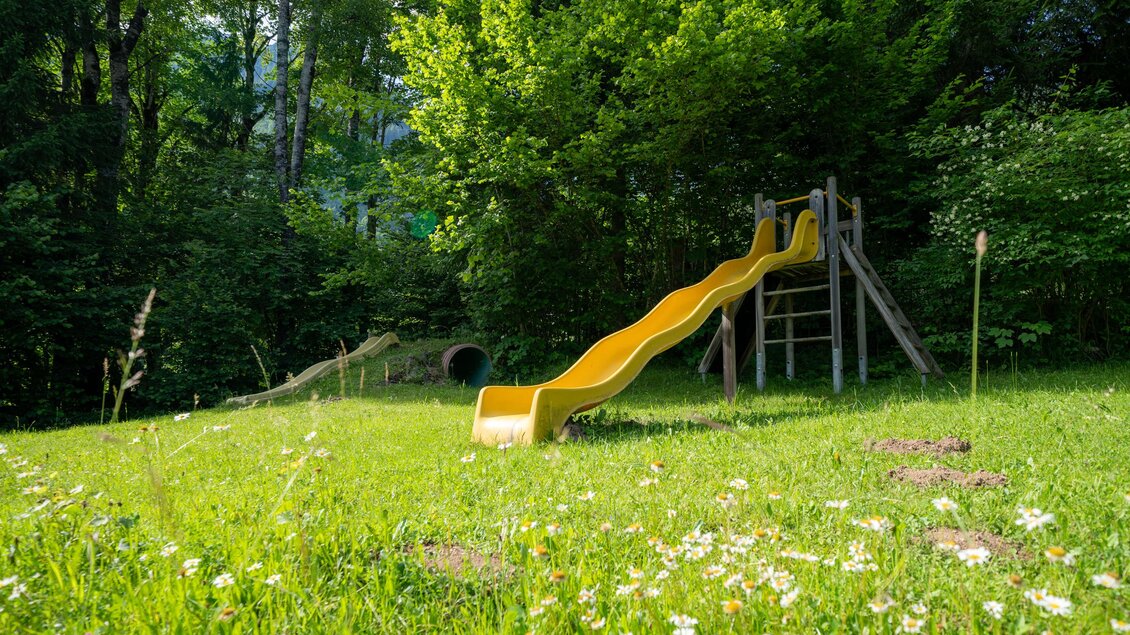 Spielplatz vom Lodenwalker Ramsau mit einer gelben Rutsche und einer Schaukel aus Holz. | © Lodenwalker Ramsau