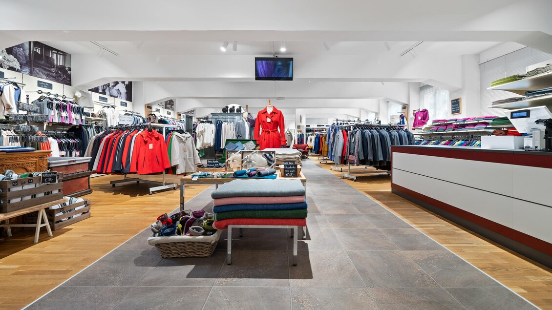 Shop Ramsau mit einer Vielzahl von Kleidungsstücken aus Loden in verschiedenen Farben. Der Raum ist hell und einladend, mit Regalen und Displays auf beiden Seiten. | © Lodenwalker Ramsau