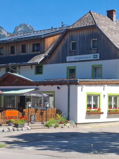 <p>Das Gasthaus Moser in Tauplitz mit großer Terrasse und roten Sonnenschirmen. Im Hintergrund ist eine grüne Landschaft und ein klarer blauer Himmel zu sehen.</p> | © TVB Ausseerland Salzkammergut