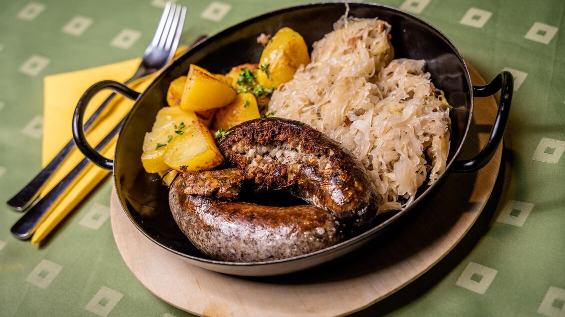 Ein traditionelles Gericht mit Würstchen, Kartoffeln und Sauerkraut. Serviert in einer flachen Schale auf einem Holzbrett. | © Stephan Friesinger