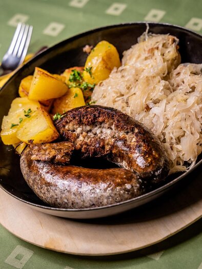 Ein traditionelles Gericht mit Würstchen, Kartoffeln und Sauerkraut. Serviert in einer flachen Schale auf einem Holzbrett. | © Stephan Friesinger