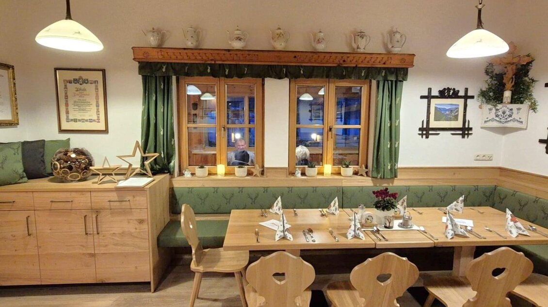 Ein gemütliches Esszimmer mit Holzmöbeln und einer langen Tafel. Die Fenster sind mit grünen Vorhängen geschmückt und Kerzen sorgen für eine warmherzige Atmosphäre. | © Gasthaus Murboden
