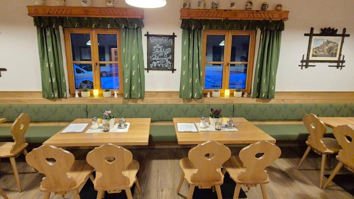 Ein gemütliches Restaurant mit Holztischen und Stühlen. Die Fenster sind mit grünen Vorhängen dekoriert und es gibt warmes Licht von Kerzen. | © Gasthaus Murbodenhüttl