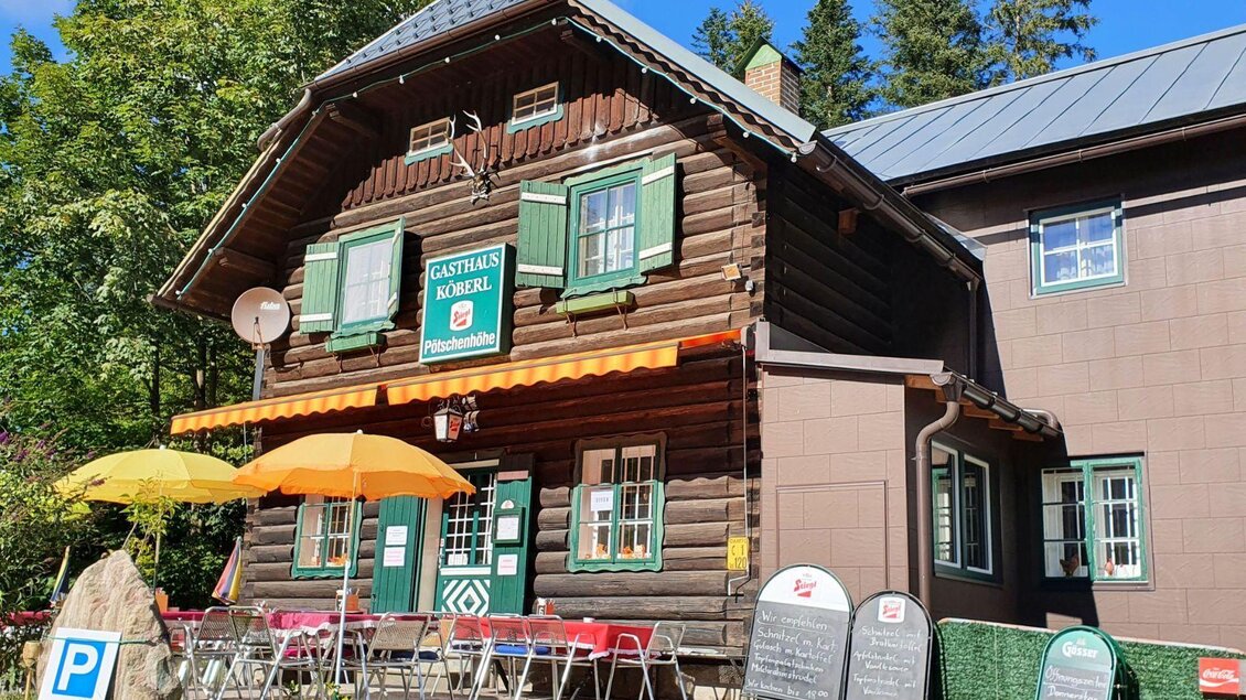 Ein gemütliches Gasthaus mit Holzfassade und grünen Fenstern. Vor dem Eingang stehen Tische mit Sonnenschirmen. | © Doris Köberl