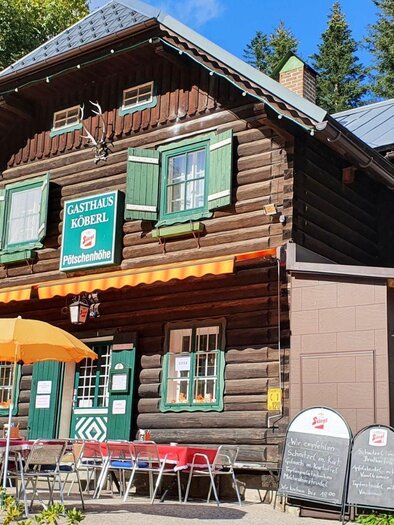 Ein gemütliches Gasthaus mit Holzfassade und grünen Fenstern. Vor dem Eingang stehen Tische mit Sonnenschirmen. | © Doris Köberl