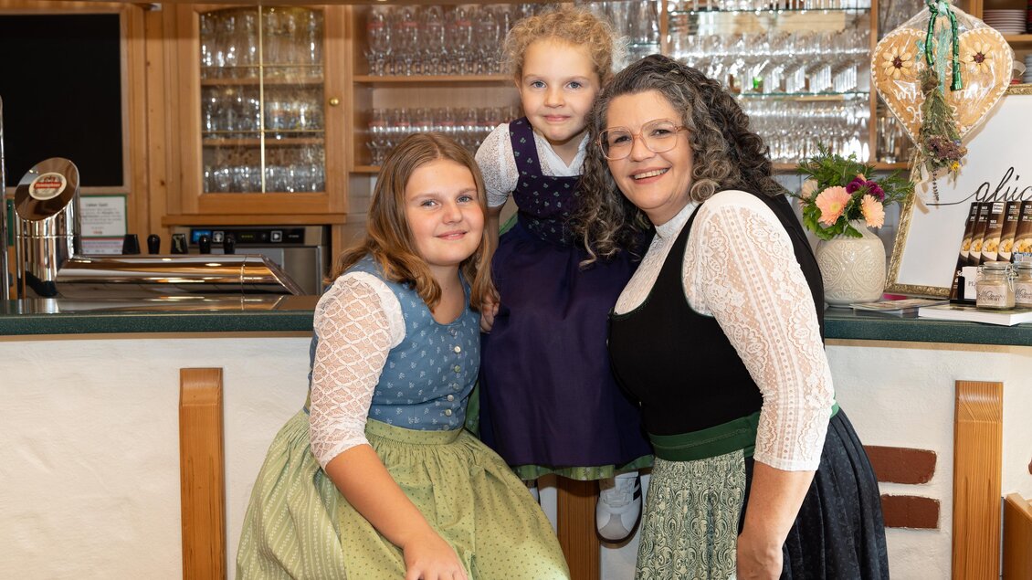 Drei Mitglieder der Gastgeberfamilie in Tracht im Schankbereich des Platzwirts in Graden.  | © Region Graz, Harry Schiffer