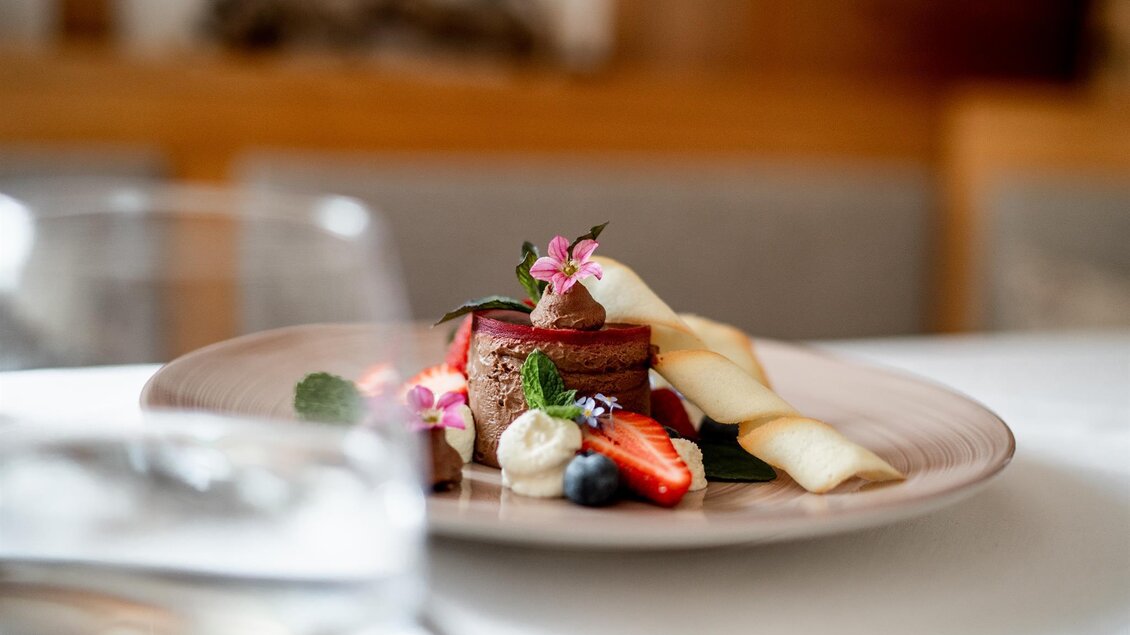 Dessert mit Beeren, Creme, Hippenröllchen und Blütendeko auf einem Teller angerichtet beim Platzwirt in Graden. | © Platzwirt_KerstinFotografie