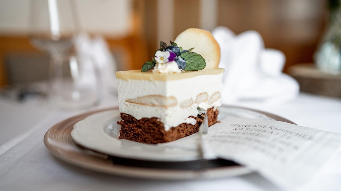 Stück Topfen-Joghurt-Torte mit Schokoboden und Blütendeko auf einem gedeckten Tisch beim Platzwirt in Graden.  | © Platzwirt_KerstinFotografie