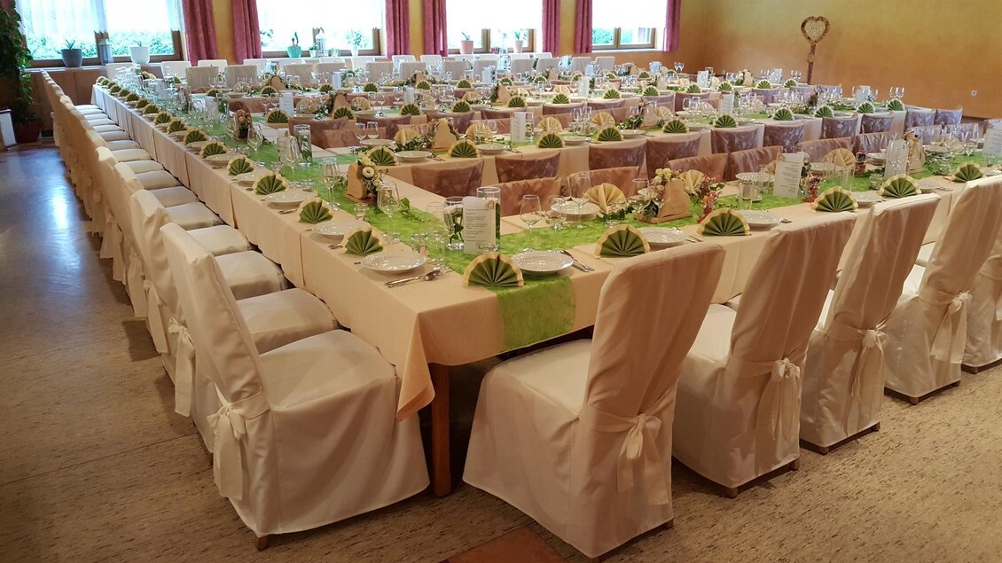 Ein festlich gedeckter Tisch in einem großen Raum, mit weißen Stühlen und dekorativen Elementen. Die Tafel ist sorgfältig vorbereitet für eine größere Veranstaltung. | © Gasthaus Rüf-Peterwirt