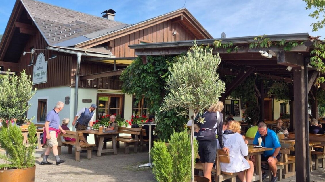 Ein gemütliches Restaurant mit Außensitzplätzen und blühenden Pflanzen. Menschen genießen ihr Essen unter einem klaren Himmel. | © Bettina Scheck