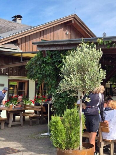 A cozy restaurant with outdoor seating and blooming plants. People are enjoying their meals under a clear sky. | © Bettina Scheck