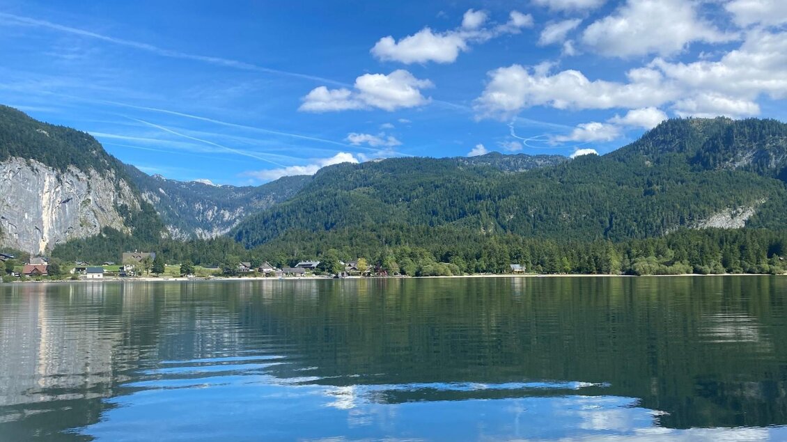 Ein klarer See, umgeben von beeindruckenden Bergen und üppigem Grün. Der Himmel ist blau mit einigen Wolken, und die Wasseroberfläche spiegelt die Landschaft wider. | © Bettina Scheck