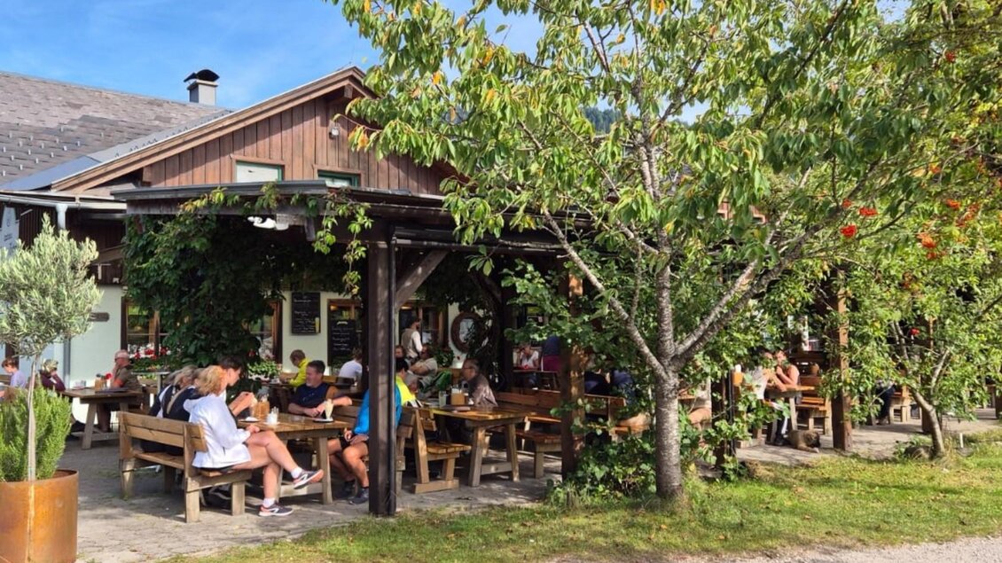 Ein gemütliches Restaurant im Freien mit Holzplätzen und Bäumen. Gäste genießen die Sonne und die entspannte Atmosphäre. | © Bettina Scheck