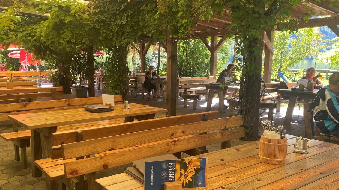 Ein einladendes Freiluftrestaurant mit holzernen Tischen und Bänken. Üppige Pflanzen und Licht sorgen für eine gemütliche Atmosphäre. | © Bettina Scheck
