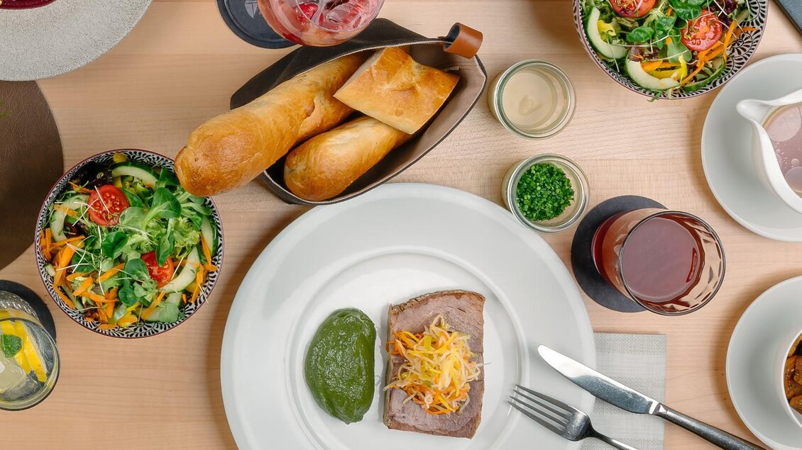 Ein dekorierter Tisch mit verschiedenen Speisen. Im Vordergrund liegt ein Teller mit Fleisch, grünem Püree und Käse, umgeben von Salaten und Brötchen. | © Gasthaus Seeblick, MONDI Resort