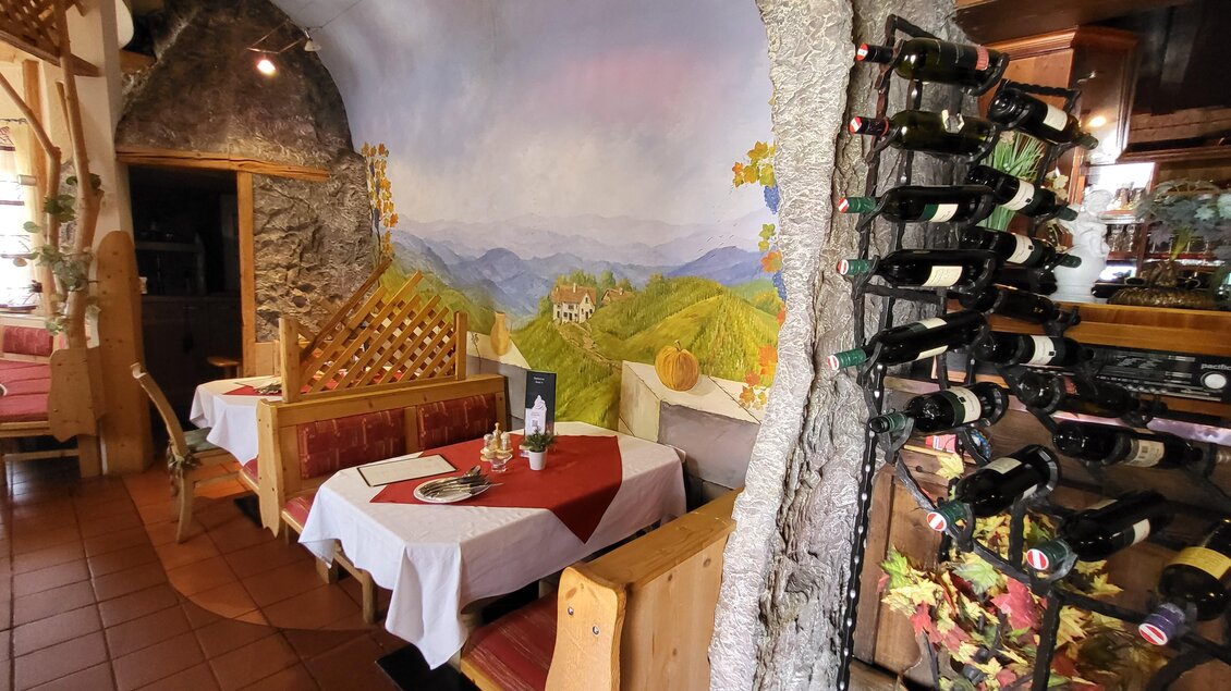 Ein gemütliches Restaurant mit Holzdekor und gedeckten Tischen. An der Wand ist ein malerisches Landschaftsmotiv zu sehen, und ein Weinständer steht im Vordergrund. | © TV Hochsteiermark