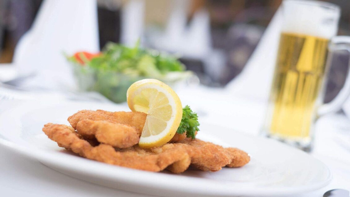 Man sieht ein Wienerschnitzel mit einer Zitrone garniert am weiß gedeckten Tisch serviert.  | © Philipp Seid