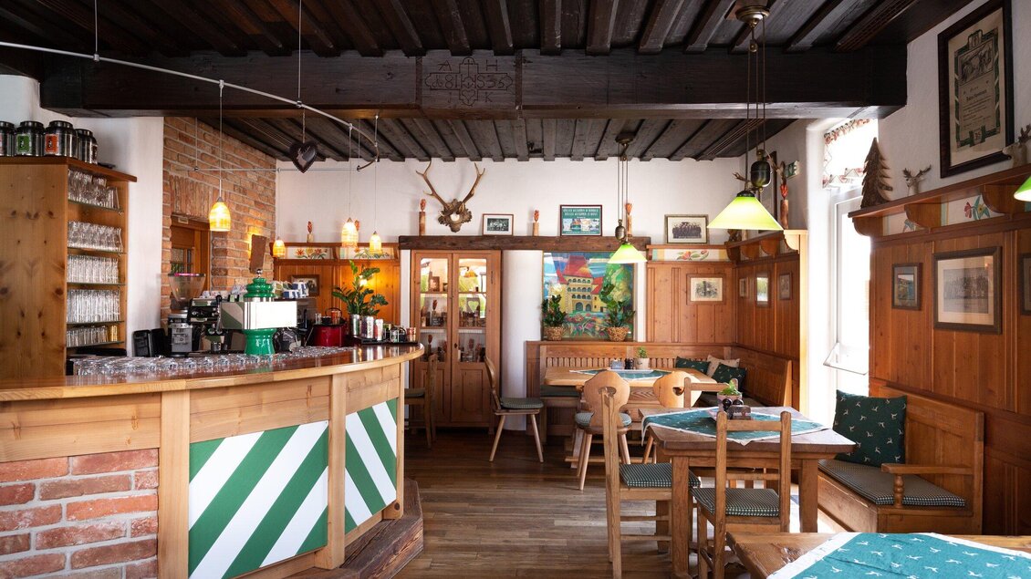 <p>Innenansicht des Gasthaus Tax in Bärnbach mit einem rustikalen Barbereich, Holztischen und traditioneller Dekoration wie Hirschgeweihen und Bildern an den Wänden, die eine gemütliche Atmosphäre schaffen.</p> | © Geopho