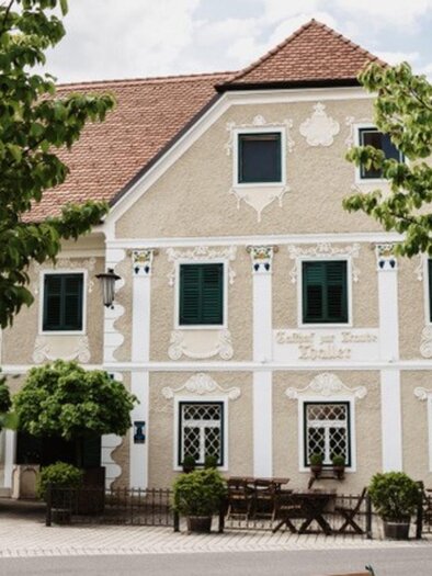 Ein charmantes Haus mit einer hellen Fassade und grünen Fenstern. Umgeben von Bäumen und Sträucher, bietet es eine einladende Atmosphäre. | © GH Thaller