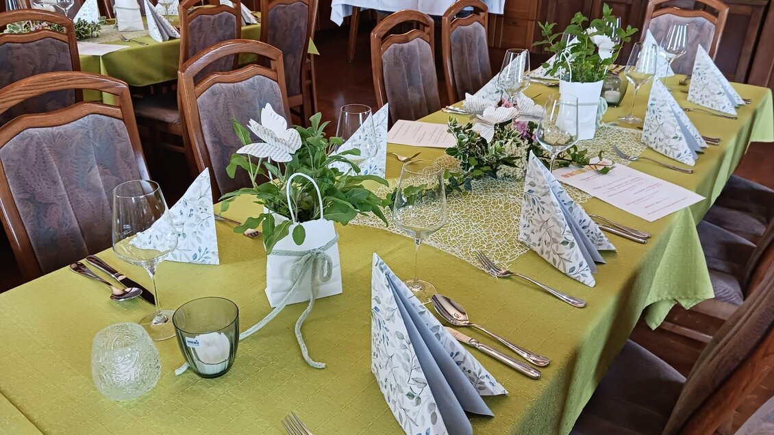 Ein festlich gedeckter Tisch in einem Restaurant mit grüner Tischdecke. Die Tafel ist dekoriert mit Blumen und gefalteten Servietten. | © Gasthaus Unterdechler
