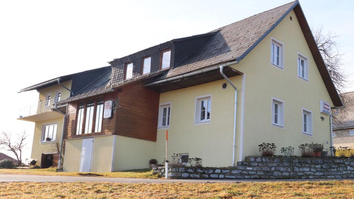 Gasthaus Wartinger in Edelschrott mit gelber Fassade, Holzbalkon und Wiese im Vordergrund | © Steirische Rucksackdörfer