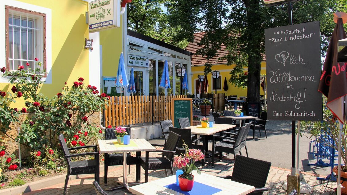 Ein einladendes Gasthaus mit einem schönen Außenbereich. Tische sind mit Blumen dekoriert und es gibt einen Schiefer mit einer Begrüßungsnachricht.