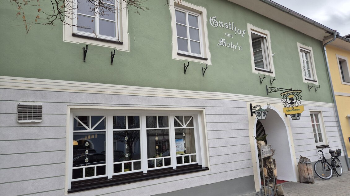 Ein Gasthof mit einer grünen Fassade und weißen Fenstern. Vor dem Gebäude steht ein Fahrrad und es gibt einen einladenden Eingangsbereich. | © TV Murau