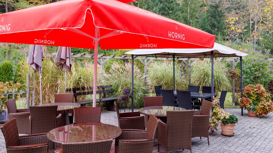 Gastgarten des Gasthofs Herlwirt in Ligist, Steiermark, mit Sitzgruppen unter rotem Sonnenschirm und Pflasterterrasse. | © TV Region Graz - Harry Schiffer