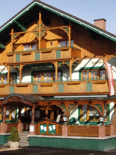 Der Gasthof Kirchenwirt befindet sich in der unteren Etage vom einem traditionellen, mehrstöckigen Gebäude mit Holzverzierungen im alpenländischen Stil. Der Kirchenwirt hat eine überdachte Terasse mit Glasgeländer.  | © Hilde Ladreiter